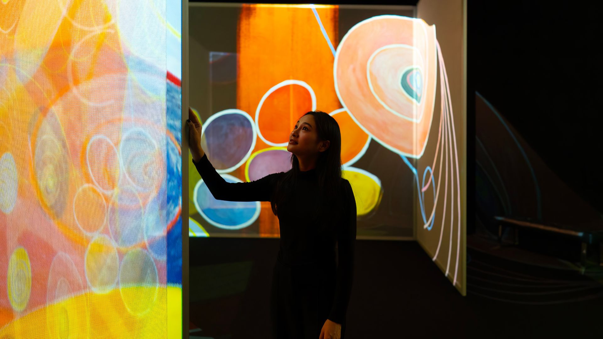 Step inside art itself at FRAMELESS in London. Image courtesy of FRAMELESS. A woman stands in an immersive gallery enjoy the abstract art installations.