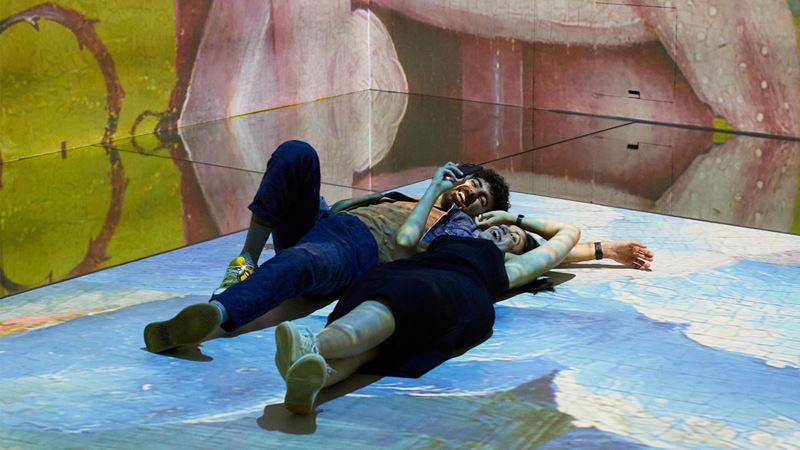 Explore art after-hours at FRAMELESS Lates. Image courtesy of FRAMELESS. Two people laying on floor surrounded by immersive art on walls and floor.