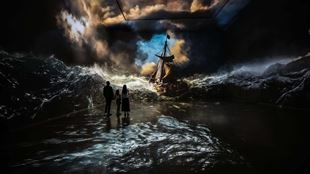 Three visitors stand inside an immersive gallery as Rembrandt's The Storm on the Sea of Galilee is projected across the walls and floor.