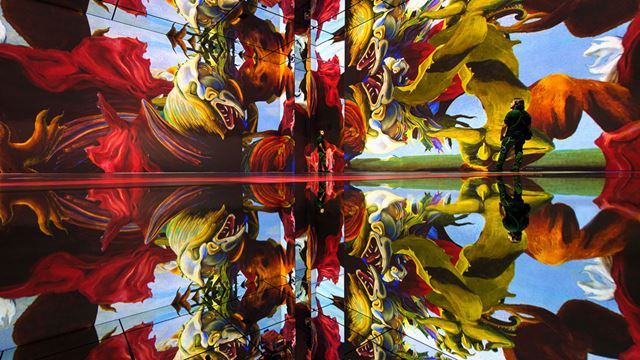 Two people are walking in a room at Frameless where a painting is projected on all four walls.