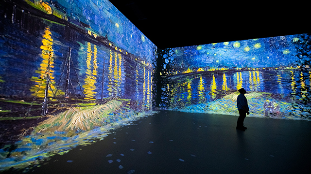 Un homme se tient dans une galerie entourée de quatre écrans et observe le tableau "Starry Night Over The Rhone" de Van Gogh à l'exposition Frameless à Londres.