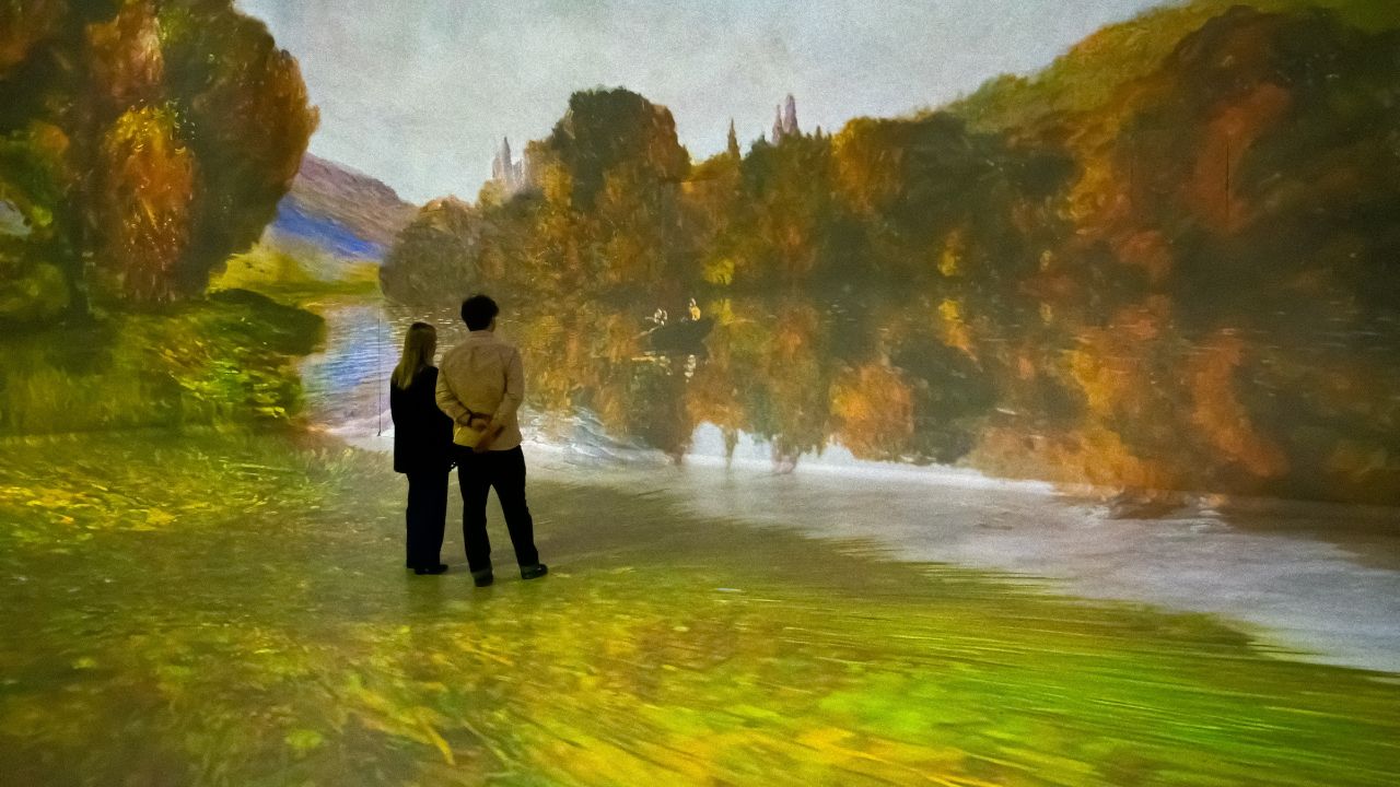Zwei Personen stehen in einer immersiven Galerie vor dem Gemälde „Rowbow on the Seine“ von Monet.
