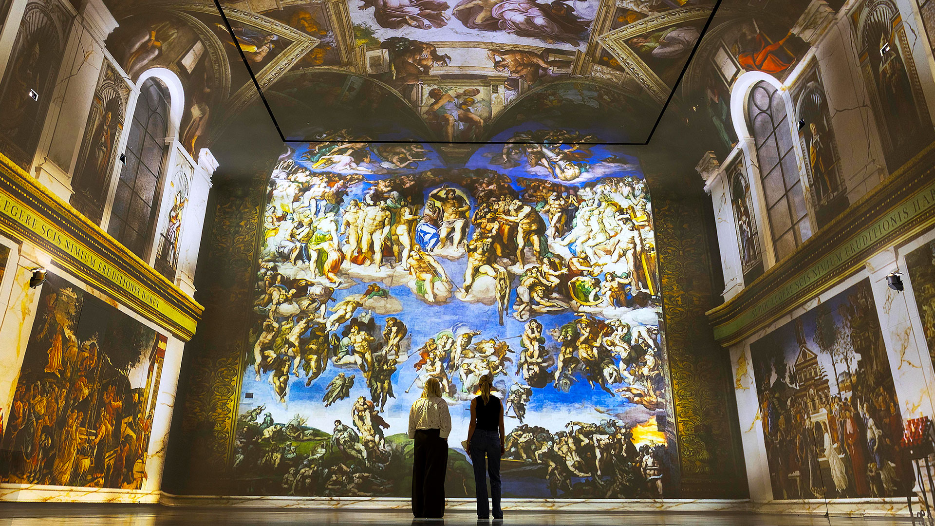 Two people are admiring one of FRAMELESS's galleries, which has been transformed into the Sistine Chapel with projections of Michelangelo's famous frescoes.