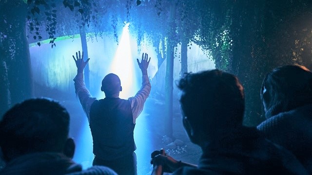 Begegnung mit Außerirdischen im Wald in Jeff Waynes immersivem Theatererlebnis War of the Worlds © Layered Reality. Bild mit Genehmigung von Layered Reality. Ein Mann steht im Wald vor einem blauen Licht was von oben kommt