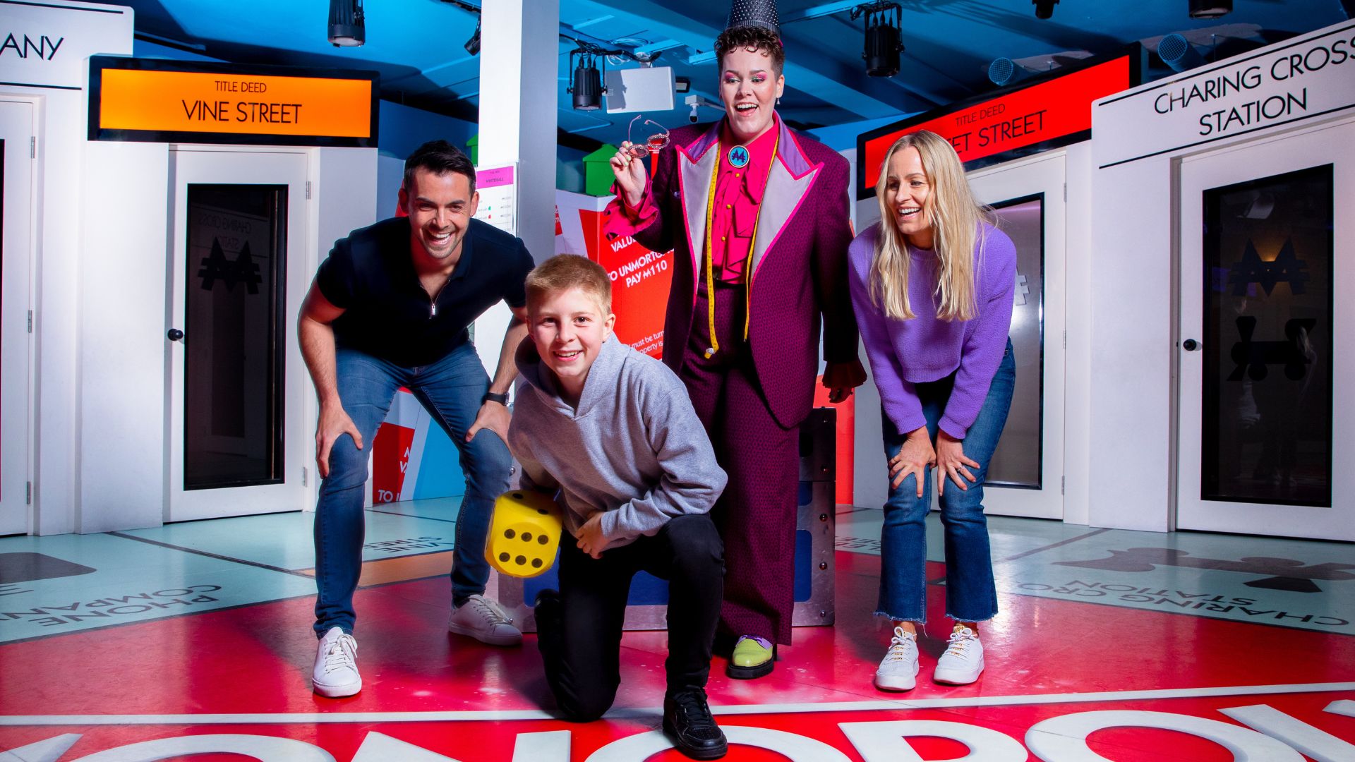 Get ready to explore London's most famous locations in the immersive experience Monopoly Lifesized. Image courtesy of Monopoly Lifesized. 3 adults and one child crouching down ready to throw a dice in an immersive experience game room