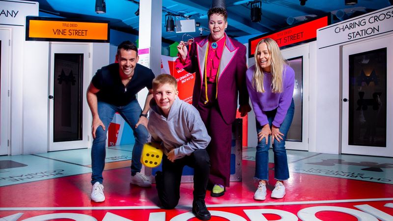 Get ready to explore London's most famous locations in the immersive experience Monopoly Lifesized. Image courtesy of Monopoly Lifesized. 3 adults and one child crouching down ready to throw a dice in an immersive experience game room