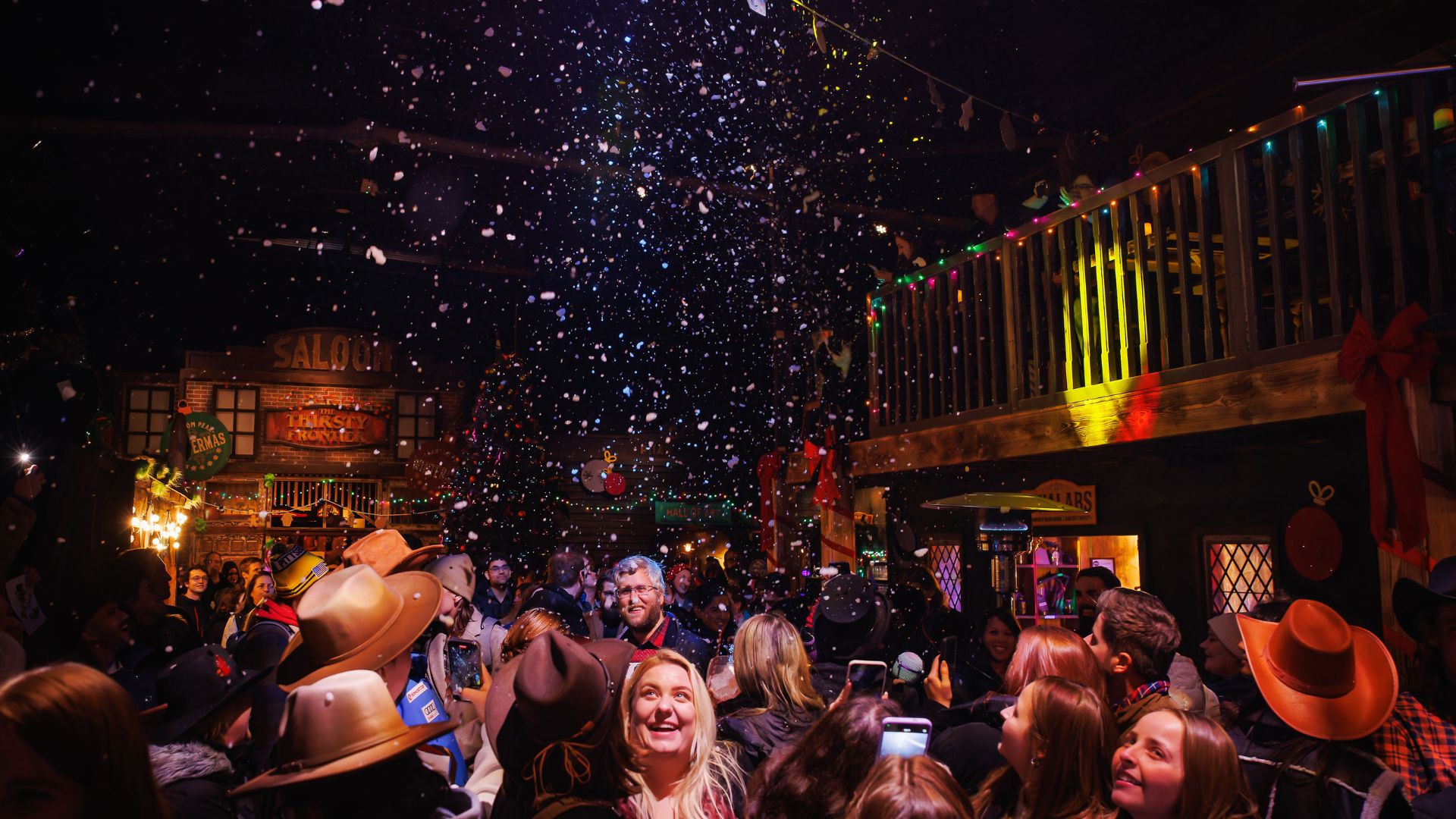 large crowed wild west theme town with fake snow falling from the ceiling and groups of people looking up and smiling