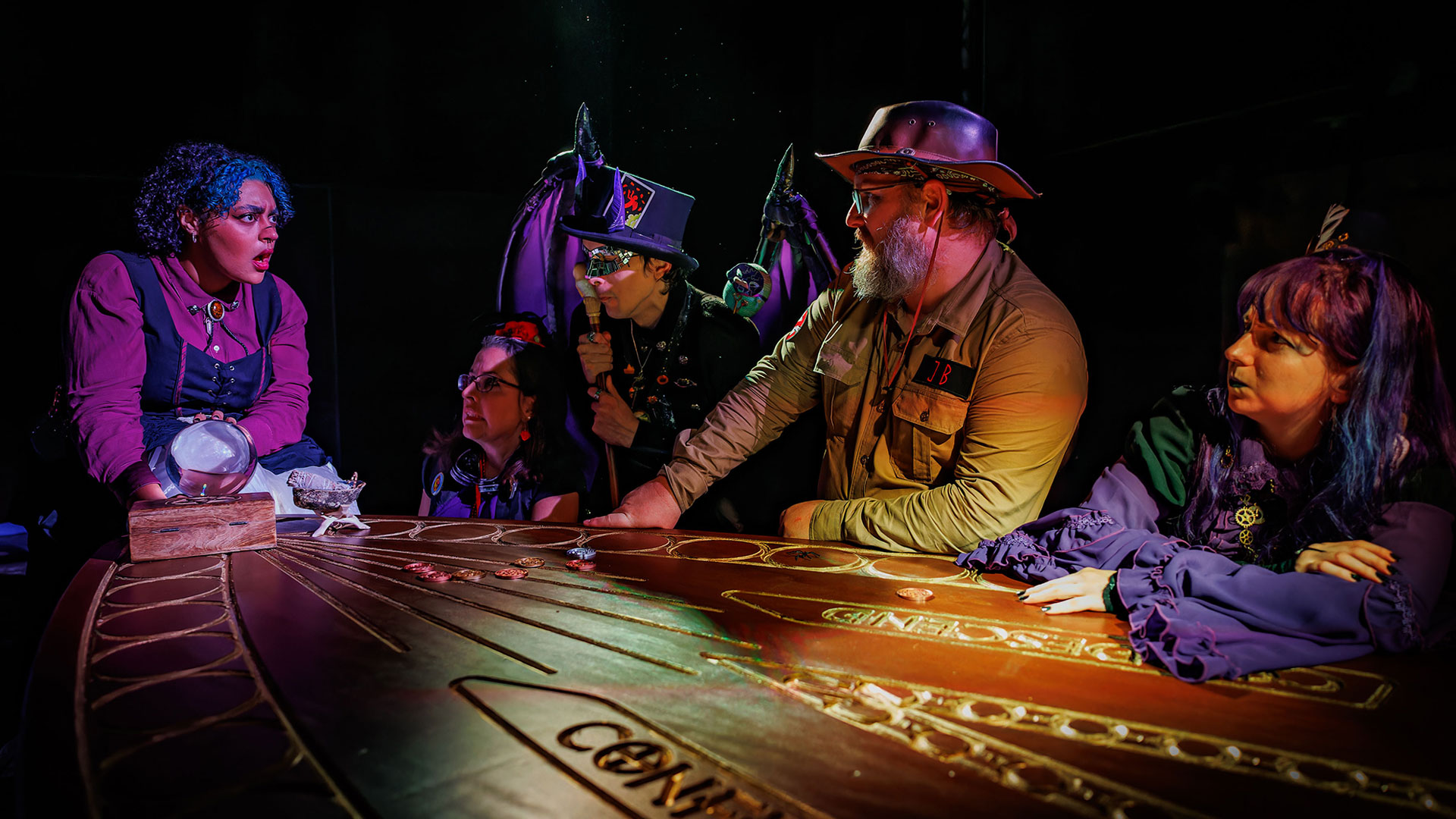Un petit nombre d'artistes, habillés tels des personnages de l'univers de Phantom Peak, sont assis autour d'une table en bois.