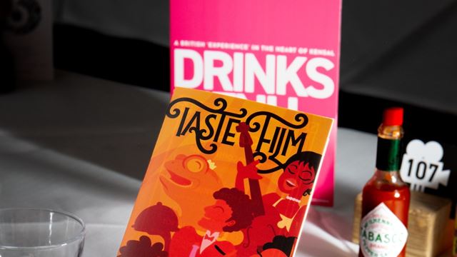 Taste Film menu card on a dining table with themed props including a hot sauce bottle and drink menu, set for an immersive cinema dining experience.