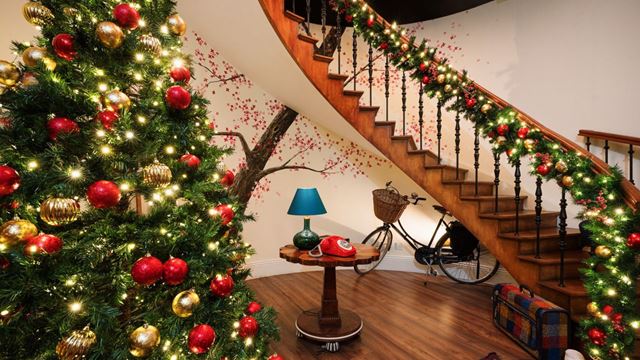 wooden floorboards and a sweeping curved staircase decorated with christmas decorations and a festive christmas tree