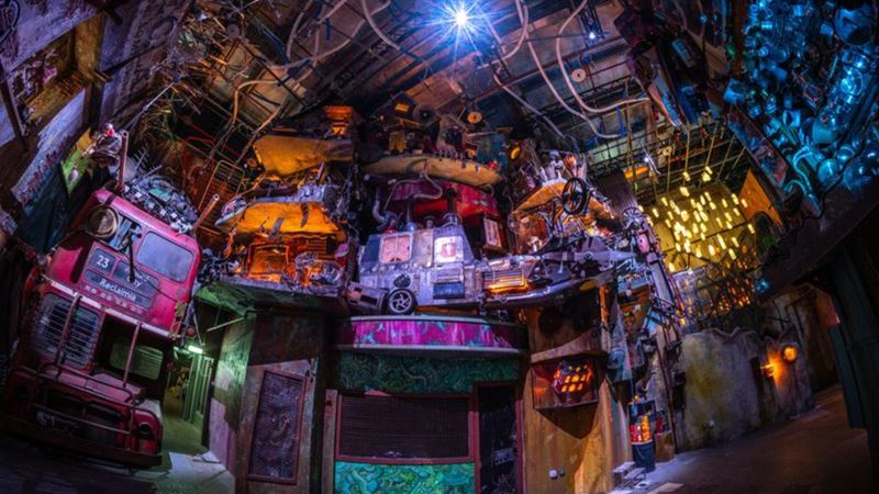 A dark, colourful room inside Wake The Tiger's Absurd City, filled with vintage vehicles, mechanical objects, colourful lights and intricate artwork.