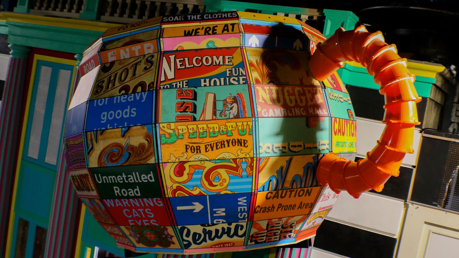 A giant colourful teapot sculpture covered in vintage-style signs and bold graphics sits inside Wake The Tiger, complete with an oversized orange spout in a whimsical immersive setting.