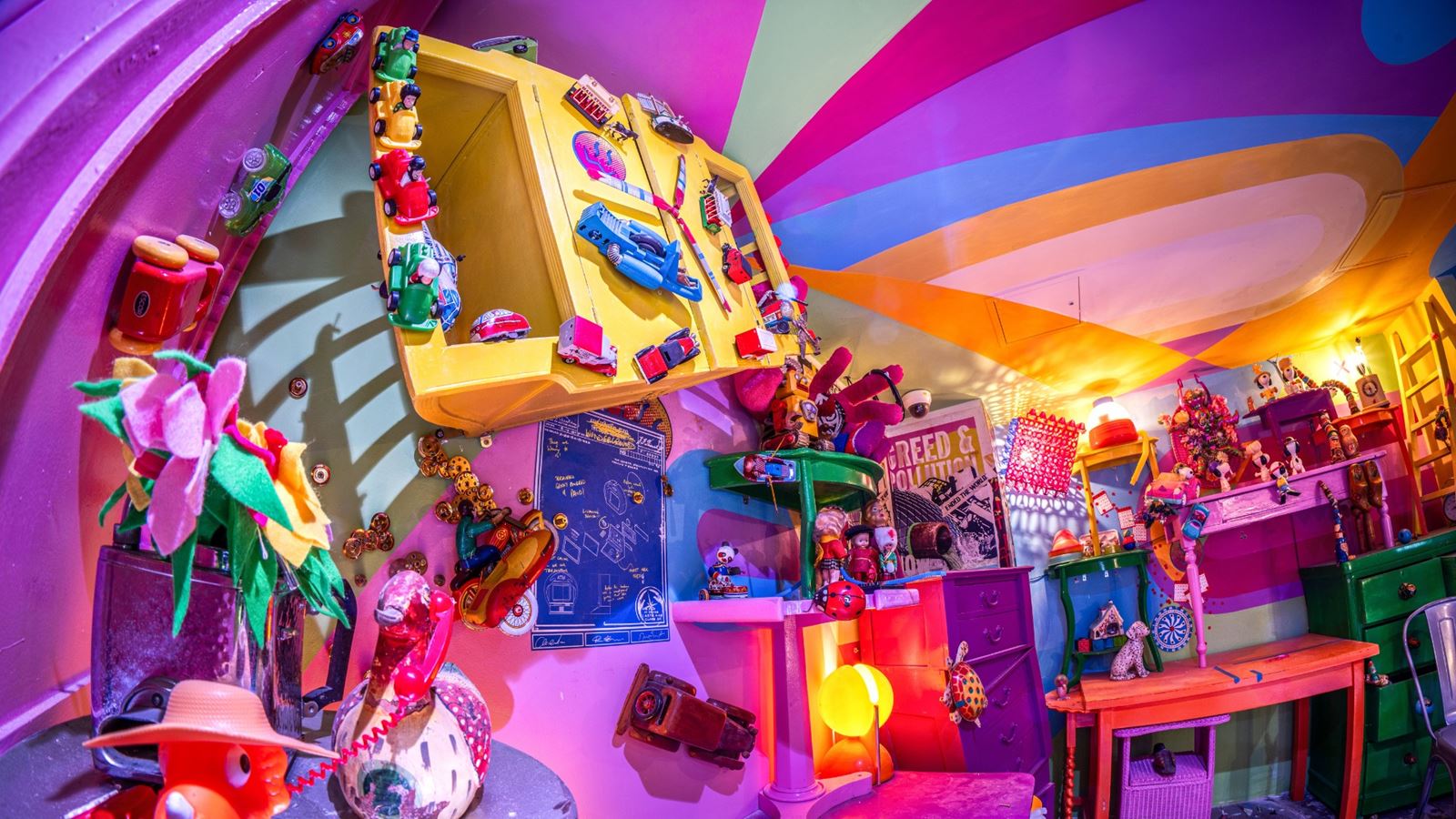 A brightly coloured room inside Wake The Tiger's immersive experience, filled with toys, artwork, colourful furniture and quirky objects beneath a rainbow-striped ceiling.