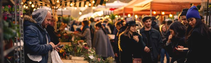 A photo of people walking through Broadway Market during winter with fairy lights in the background