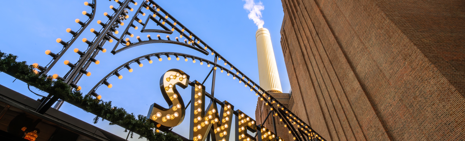 Part of Battersea Power Station building with chimney and blue sky in the background and light bulbs in the foreground.