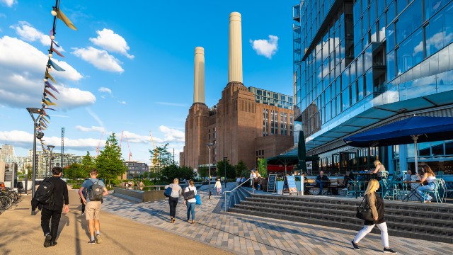 People walking in front of Battersea Power Station with blue skies behind.