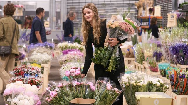 A young blond girl holding flowers and surrounded by flowers at New Covent Garden Market.