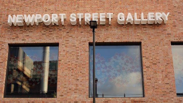 Red brick building facade with windows and white letters on the wall spelling out Newport Street Gallery.