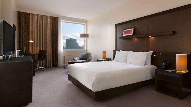 Double hotel room with bed in white sheets, brown and white walls, carpeted floors and window with view of Canary Wharf.