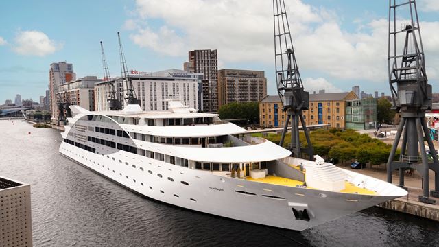 Large white yacht anchored in a harbour with blue sky and white clouds.