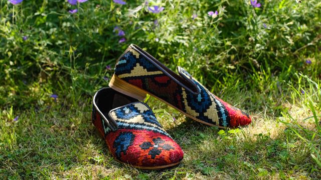 A pair of Pickett's colourful red and blue slippers made from kilim,  setagainst foliage.