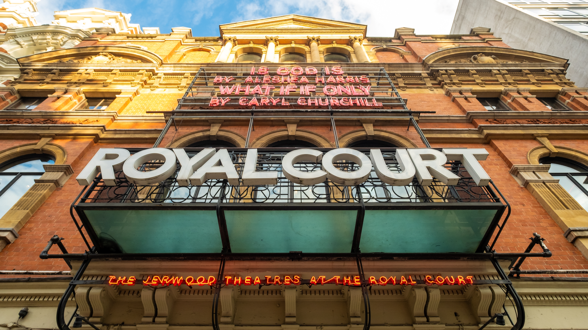 A view from the entrance of the Royal Court Theatre looking up at the building's exterior with signs of the building's name and what's on on a sunny day
