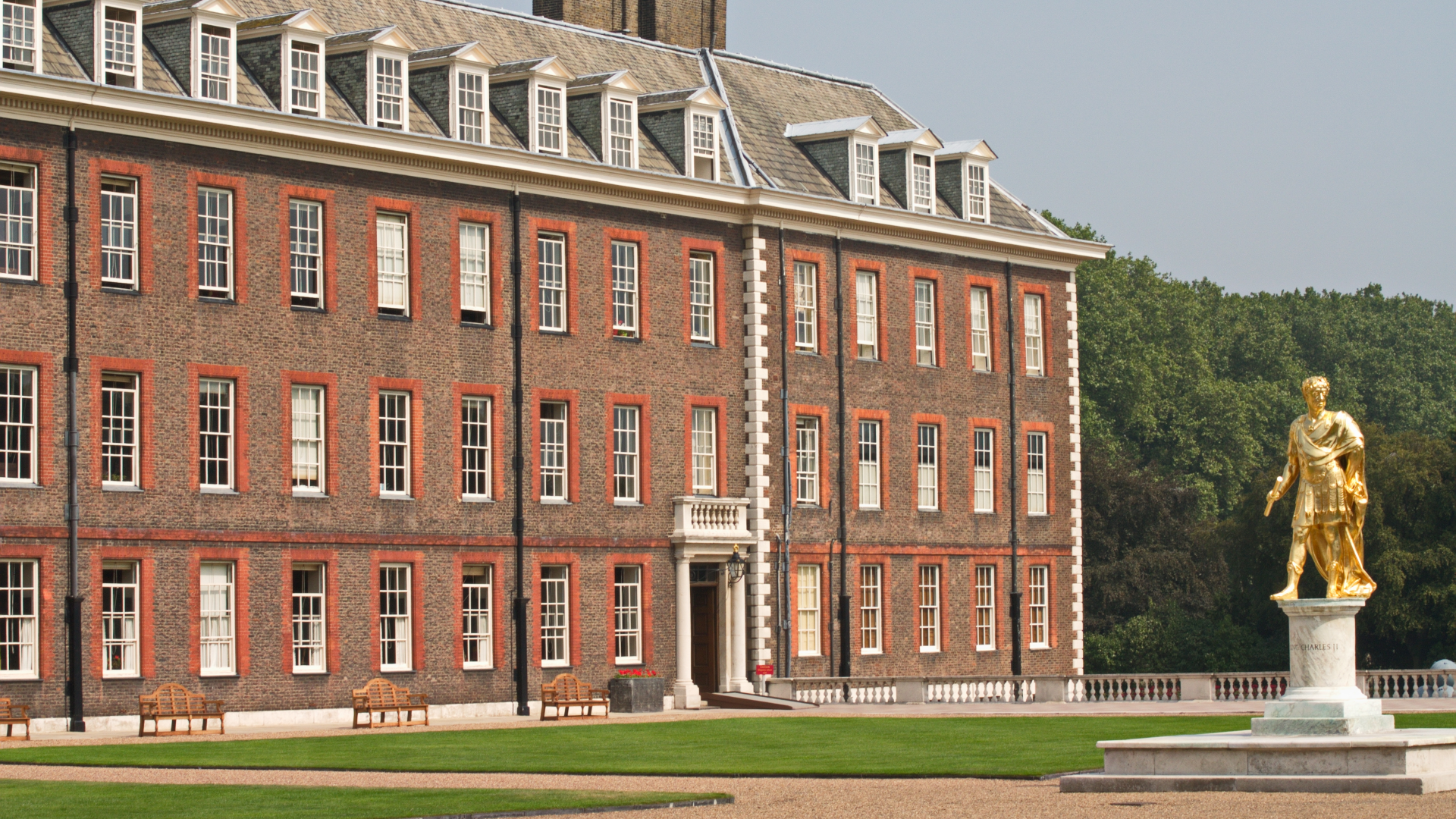 The grand Royal Hospital Chelsea building with very well maintained grass outside the front and a giant gold Statue of King Charles III