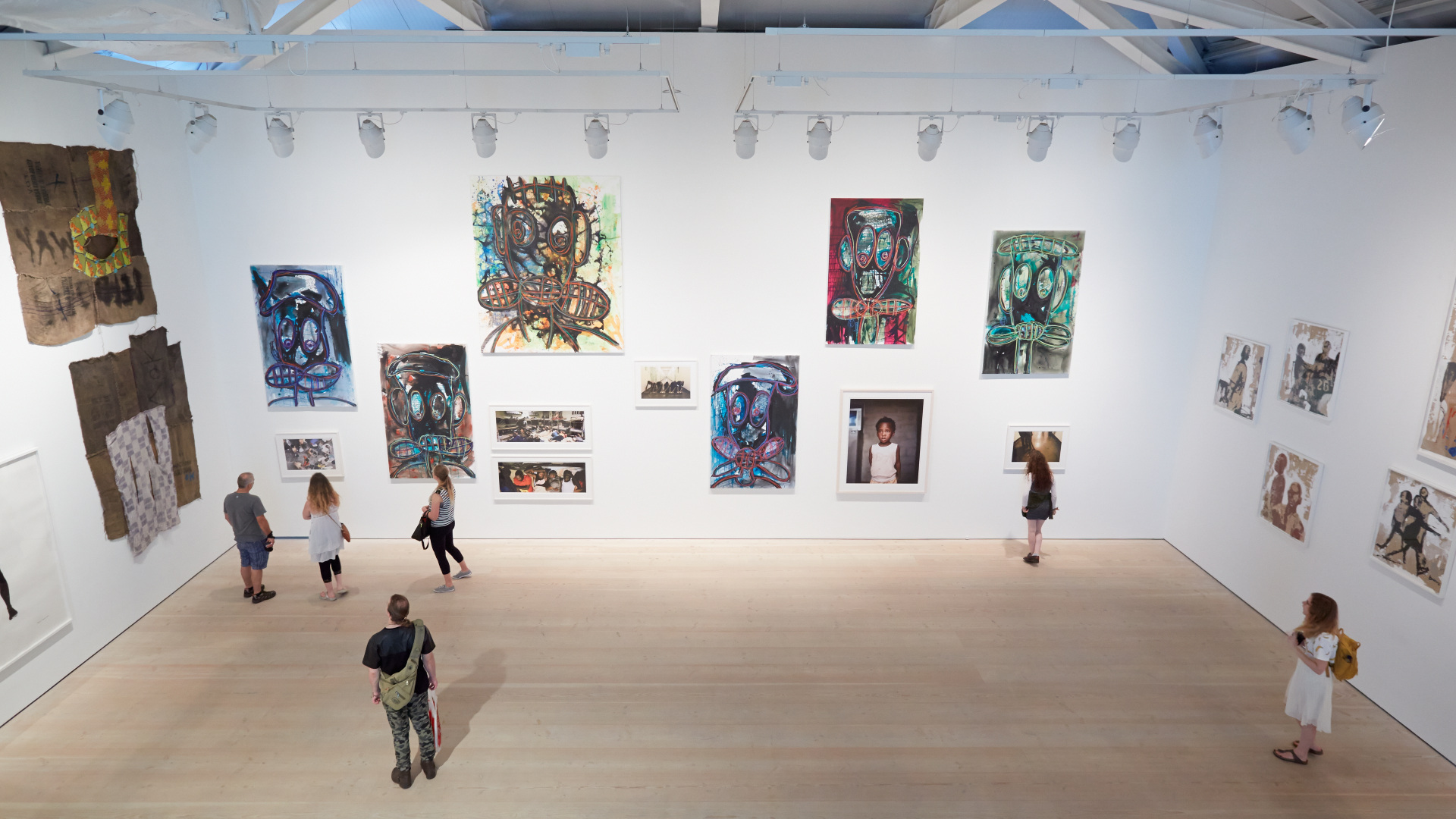 A view from inside the Saatchi Gallery looking down at people in a hall with huge white walls and wooden flooring, as they admire the artwork covering the walls