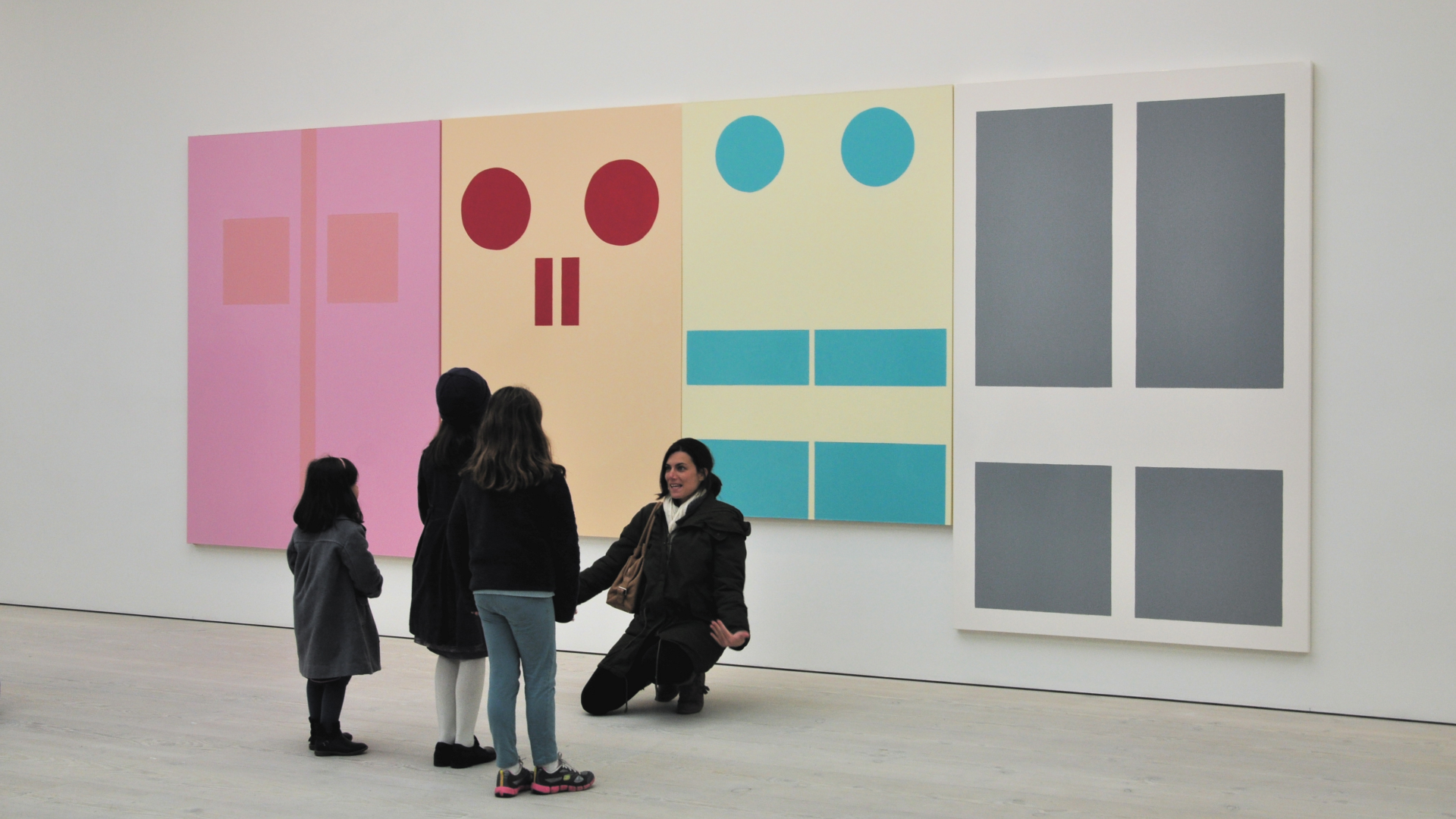 A mother kneels in front of contemporary art at Saatchi Gallery as she gestures for her three young daughters to join her for a photo