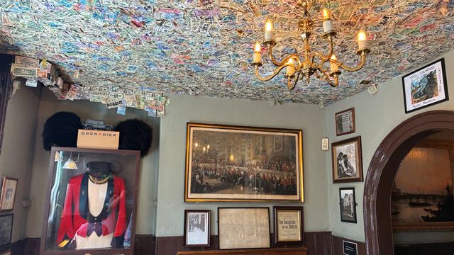 The interior of The Grenadier pub, featuring monetary notes pinned to the ceiling and a Grenadier Guards' uniform in a display case.