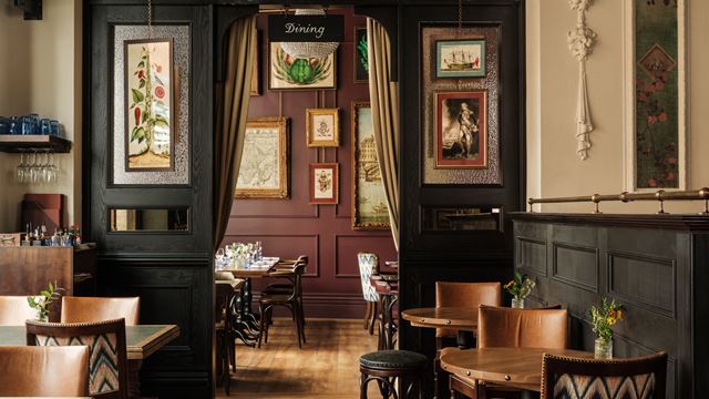 A view of the pub dining room at The Trafalgar, featuring wooden chairs and tables, and a curtain with a wood-pannelled room in the background.