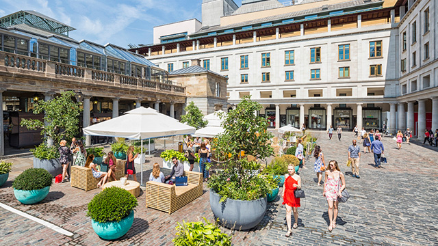 Des gens assis sur la place de Covent Garden avec des femmes se promenant au soleil.