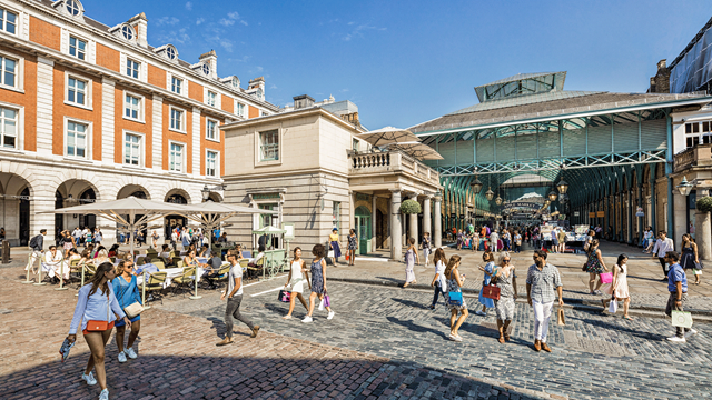 People sat on tables and walking around Covent Garden Piazza on a bright sunny day
