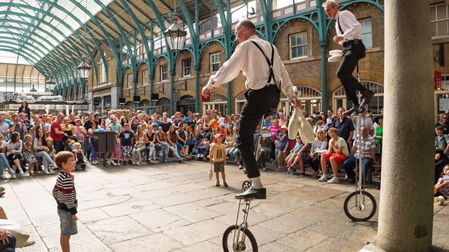 Unicycle performers entertaining a large audience inside Covent Garden Market.