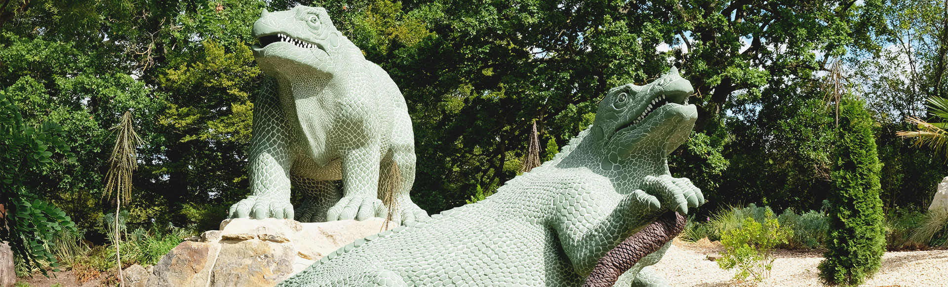 Two large green dinosaur statues, dating back to the Victorian era, are positioned on large stones within Crystal Palace Park.