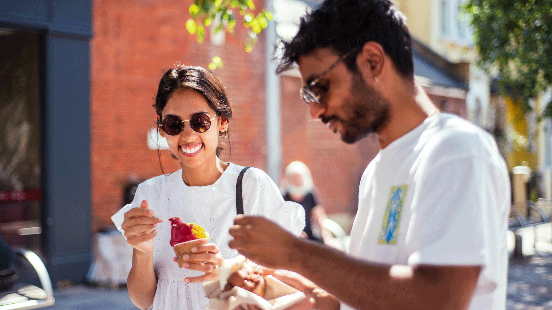 Man and woman stood smiling in the sun whilst eating ice cream