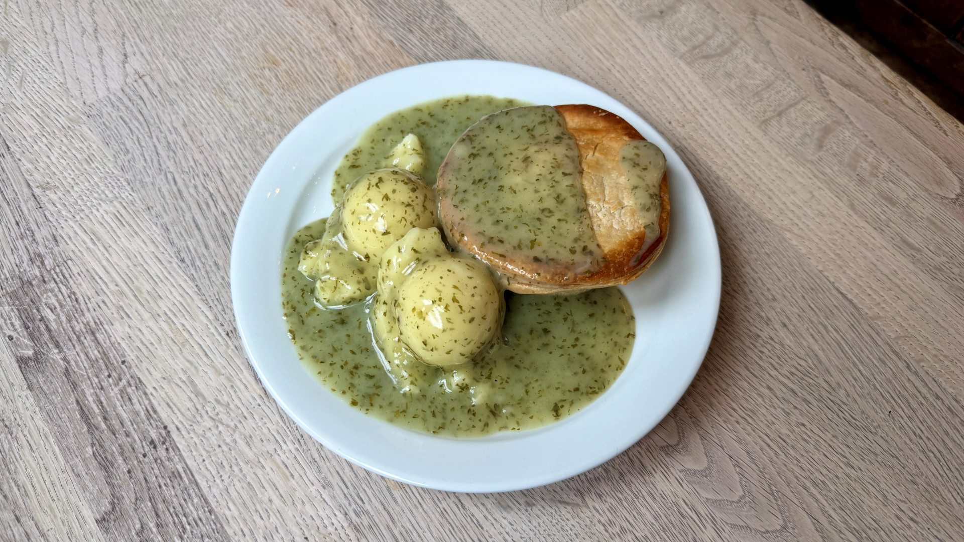 A photo of a plate of food from Goddards at Greenwich with a pie, two scoops of pie and liquor sauce