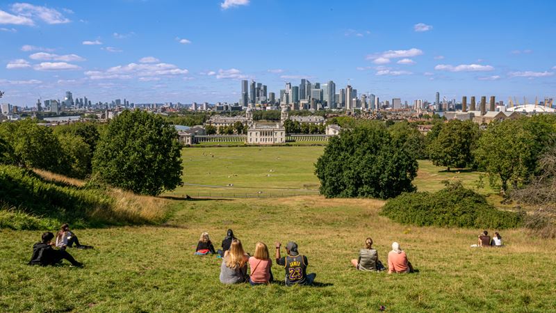 Take a wander to Greenwich Park, the oldest London royal park, and admire the view over Canary Wharf. Image credit: London & Partners/Michael Barrow. Image courtesy of London & Partners. A photo of groups of people sat on a hill at Greenwich Park overlooking London in the distance