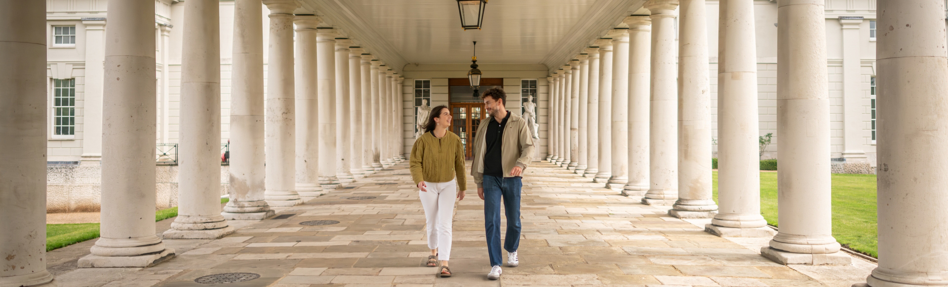 A photo of a man and woman walking between a columned walkway on the Old Royal Naval College grounds