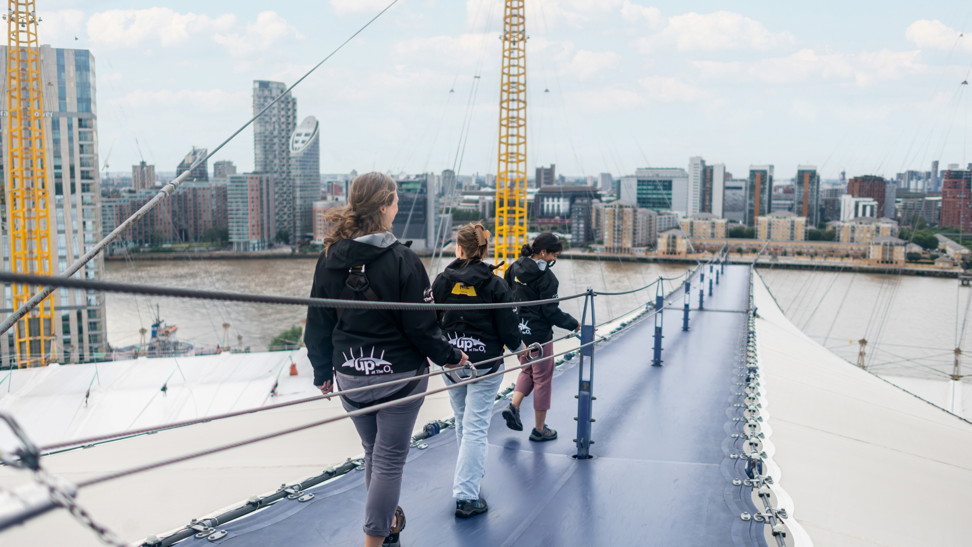 A photo of three women scaling the roof of The O2 during Up at The O2 with a backdrop of London in the background 