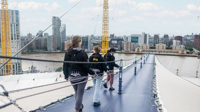 A photo of three women scaling the roof of The O2 during Up at The O2 with a backdrop of London in the background 