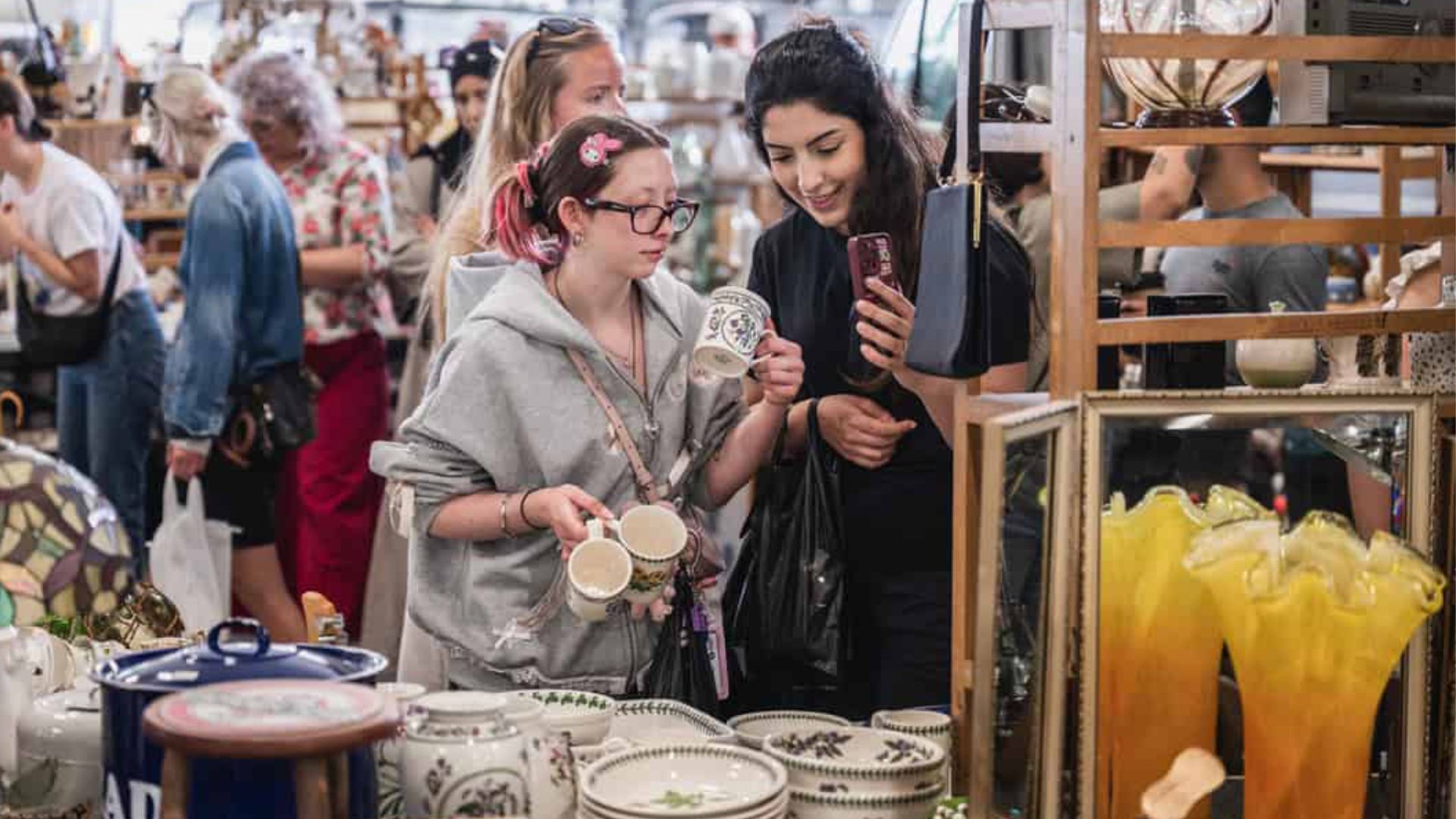 Two young women holding a pair of cream ceramic mugs at a flea market
