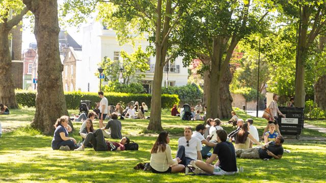 A photo of multiple groups sat on the grass in the sun at London Fields
