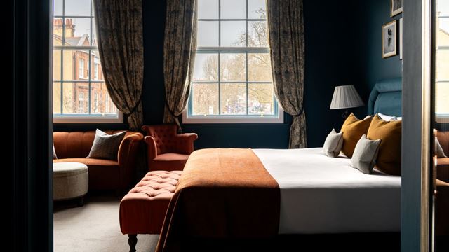 Stylish bedroom at Aragon House, featuring a large bed, dark blue walls, patterned curtains and warm orange furnishings.