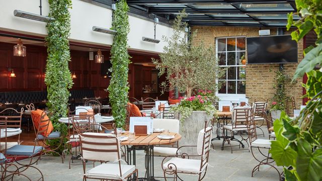 Leafy courtyard dining area at The Hound in Chiswick, with outdoor tables, plants and a covered seating area.