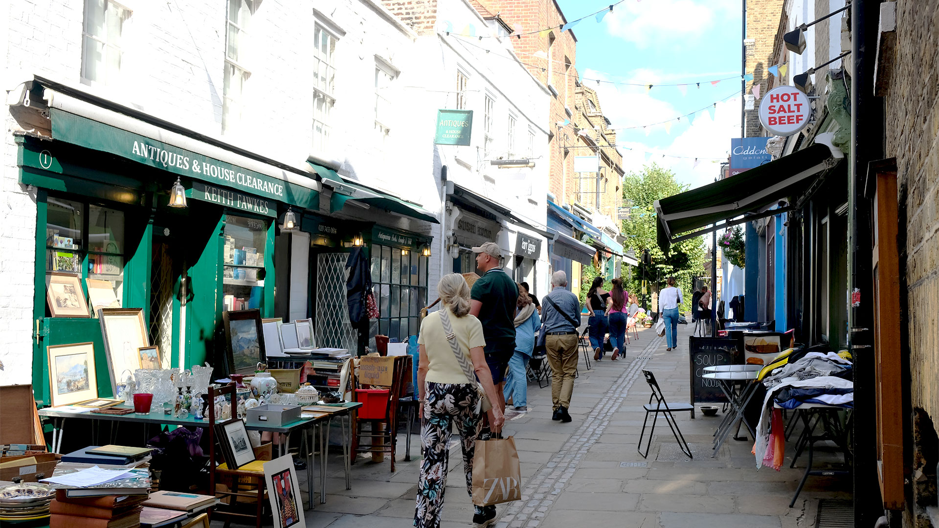Flask Walk, a cobbled alleyway lined with shops on both sides, with outdoor tables displaying vintage goods and more.
