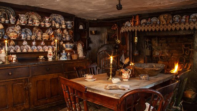 A photo of the kitchen and dining room inside Dennis Severs' House filled with Victorian-themed pottery and lit candles