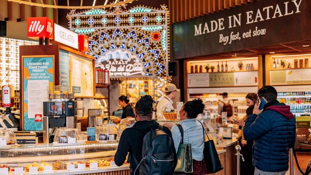 A couple stand at the counter of The Gran Caffe inside Eataly to order, with an Illy coffee and Made in Eataly sign above them