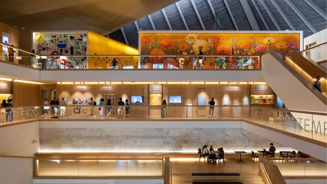 The interior of the Design Museum showcasing its various floors and a large billboard on the top floor of the Design Museum, with people walking past it.
