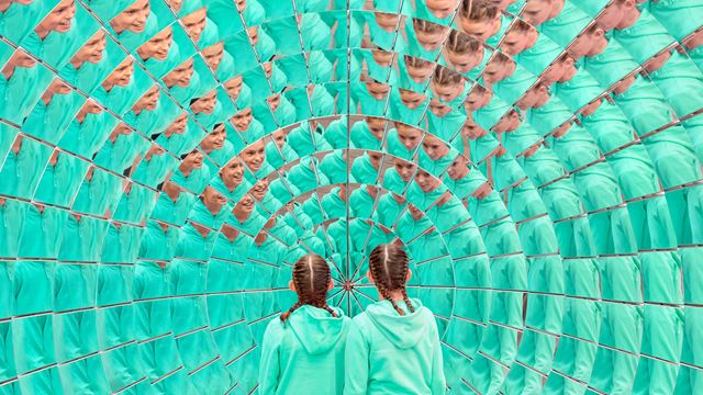 Twin girls dressed in green looking into a mirror with hundreds of reflections